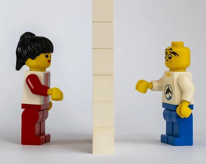 Due personaggi LEGO separati da un muro costruito con mattoncini, metafora delle difficoltà comunicative