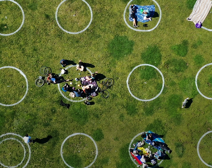 Persone sedute su un prato all’interno di cerchi tracciati per il distanziamento fisico, vista aerea. Webinar 'Design per un futuro sostenibile'.
