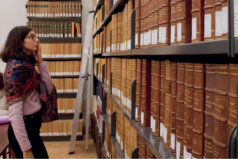 una ricercatrice cerca un testo tra gli scaffali della biblioteca fscire